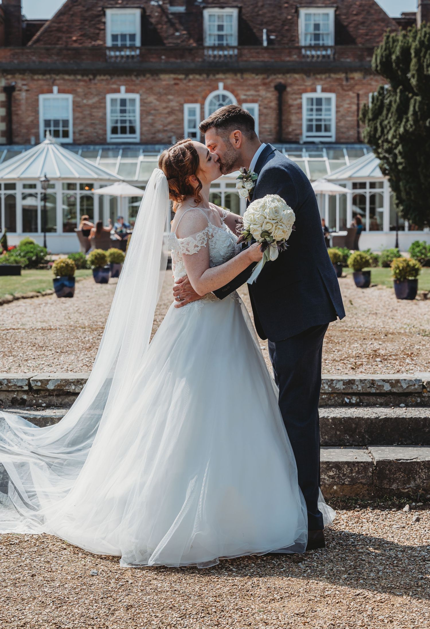 A romantic wedding moment captured outside a beautiful brick manor house with a flowing white dress and garden setting.