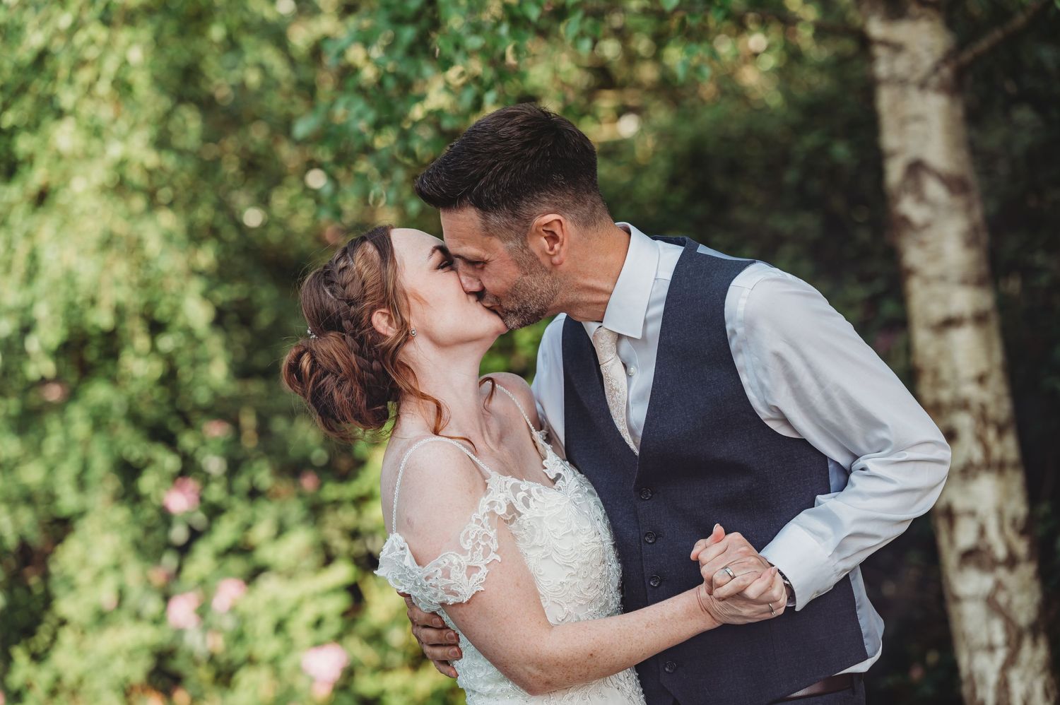 An intimate wedding moment captured outdoors with a romantic embrace against a green leafy natural backdrop.