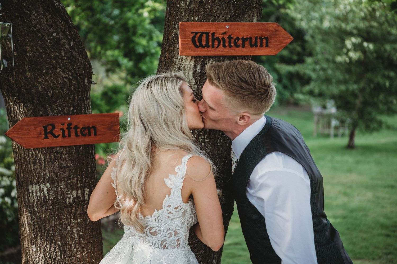 Couple kissing by rustic wooden directional signs during outdoor wedding shoot.