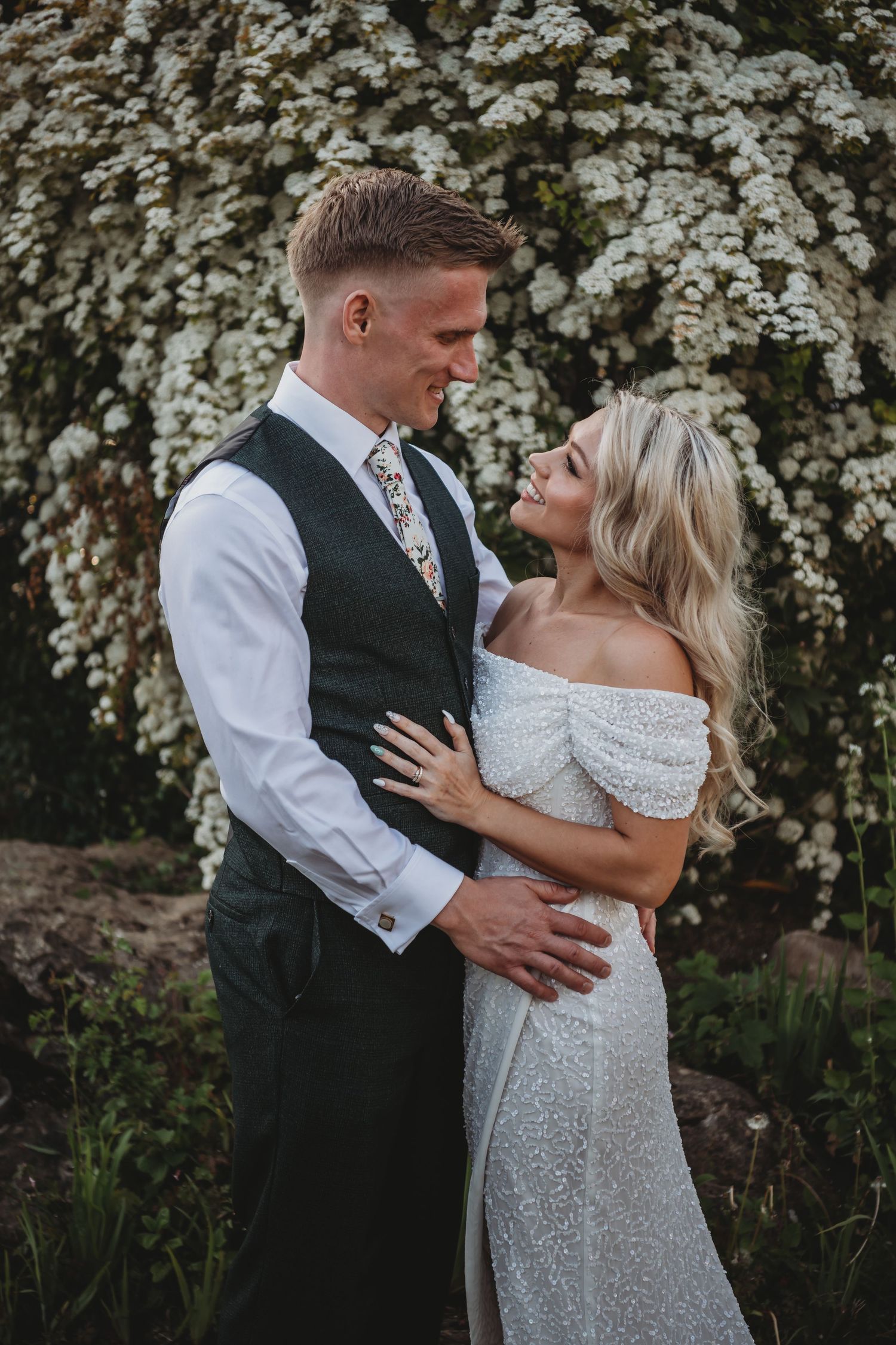 Elegant couple in wedding attire posing against blooming spring flowers.