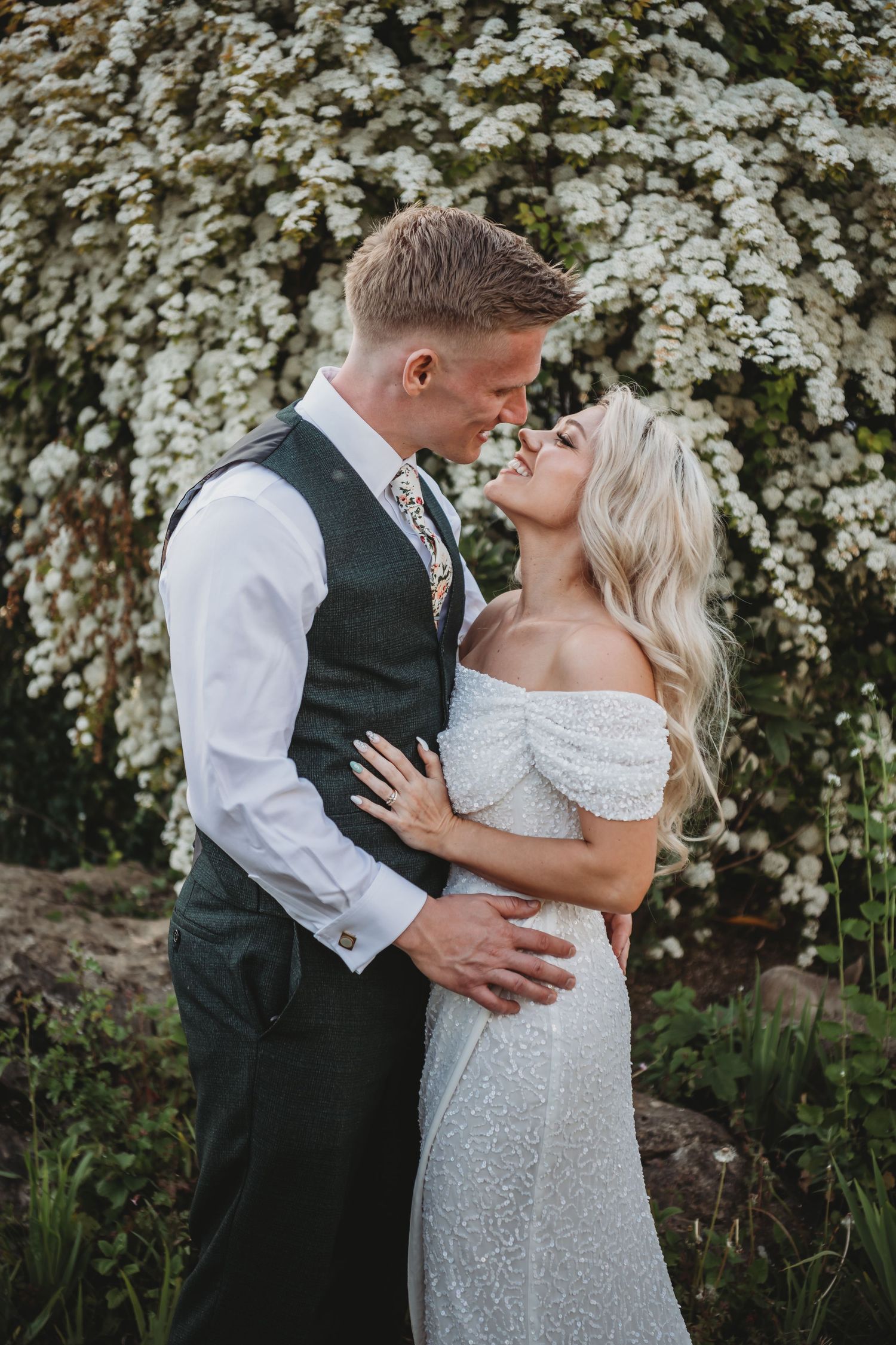 Romantic wedding portrait with couple embracing against white flowering background.