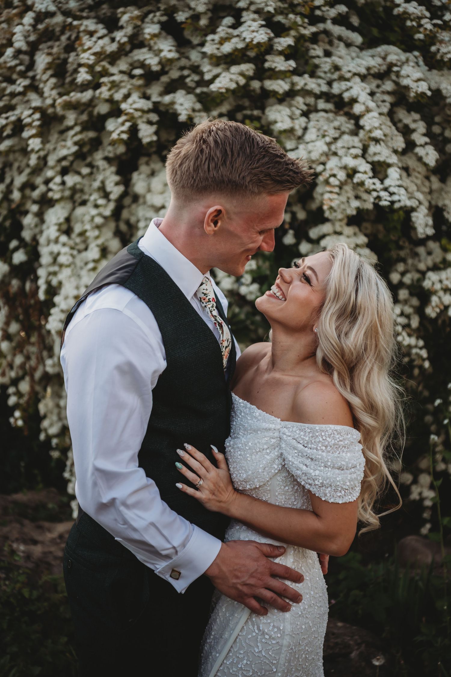 Romantic couple embracing in front of flowering bush during wedding photoshoot.