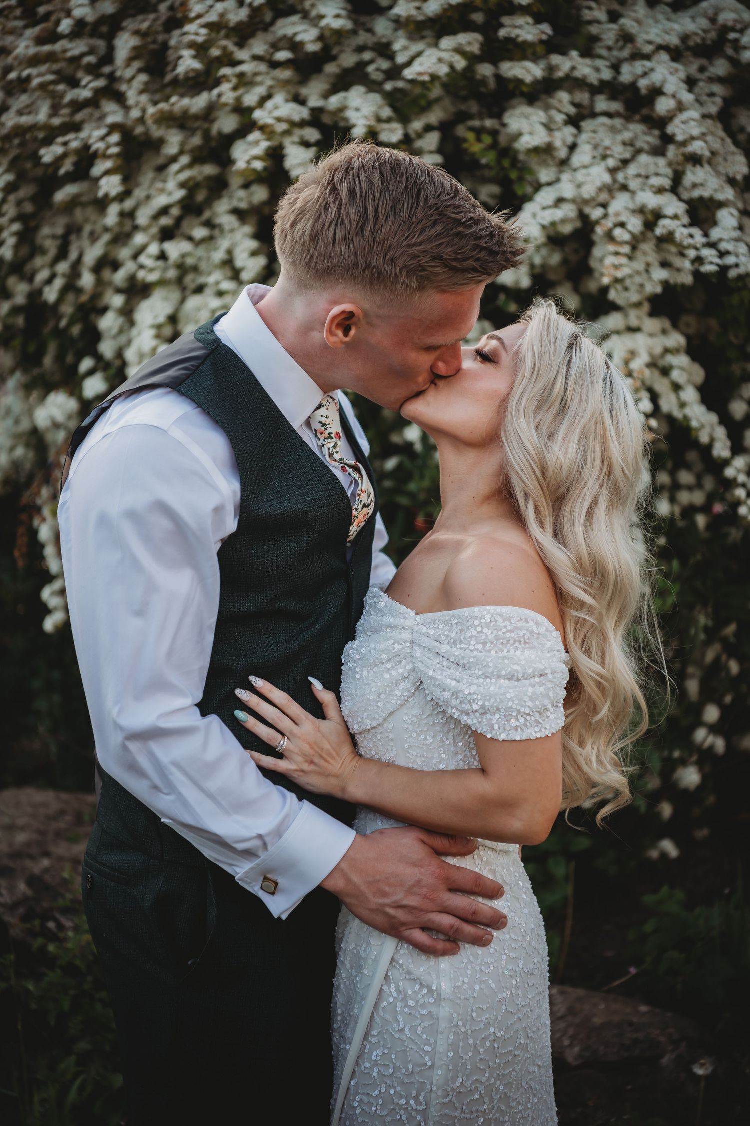 Newlywed couple sharing intimate kiss against backdrop of white flowering trees.