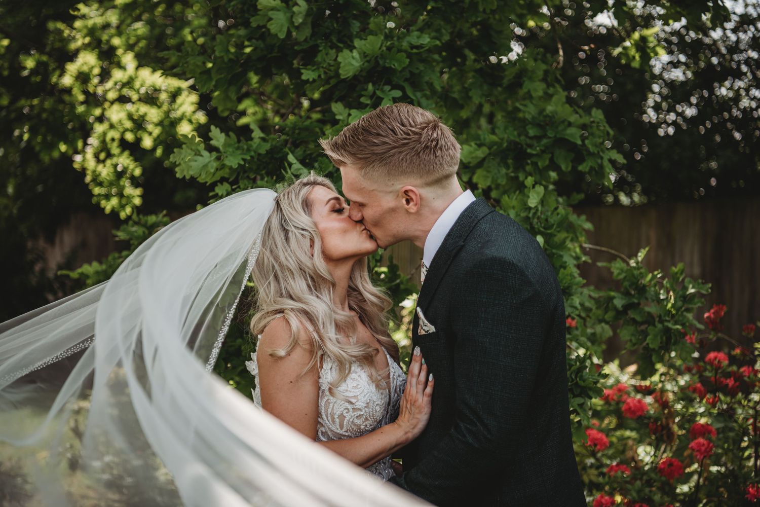 An intimate wedding portrait with flowing veil movement against a garden backdrop.