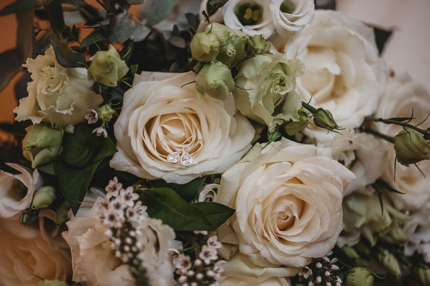 Elegant cream roses and delicate green foliage create a romantic wedding bouquet with soft textural details.