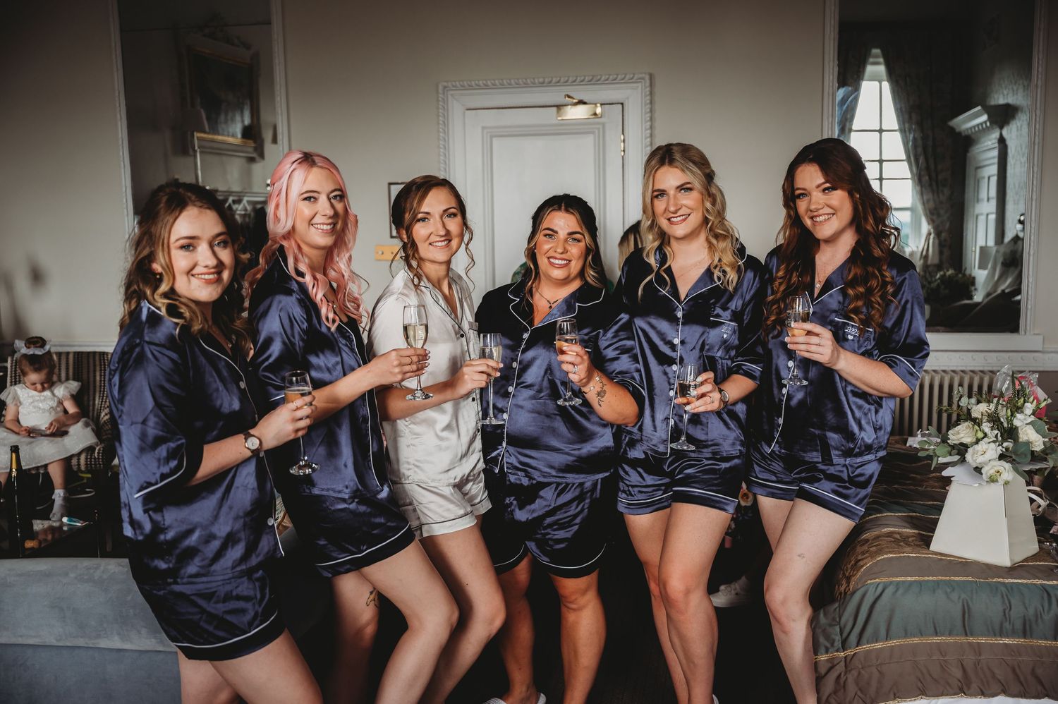 Bridal party in matching navy satin robes pose together in living room before wedding celebration.