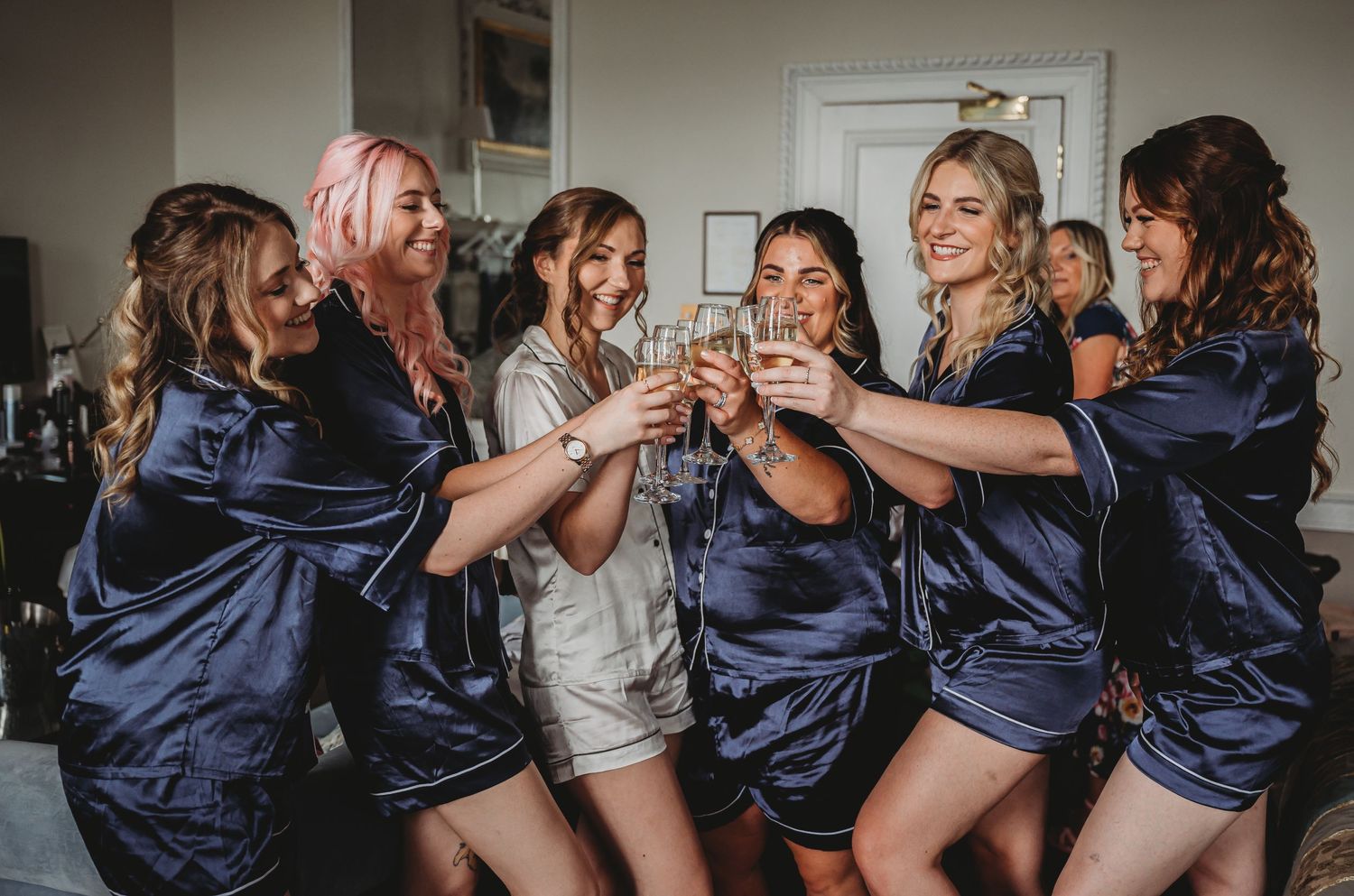 Wedding party toasts with champagne glasses while wearing matching silk robes during pre-ceremony preparations.