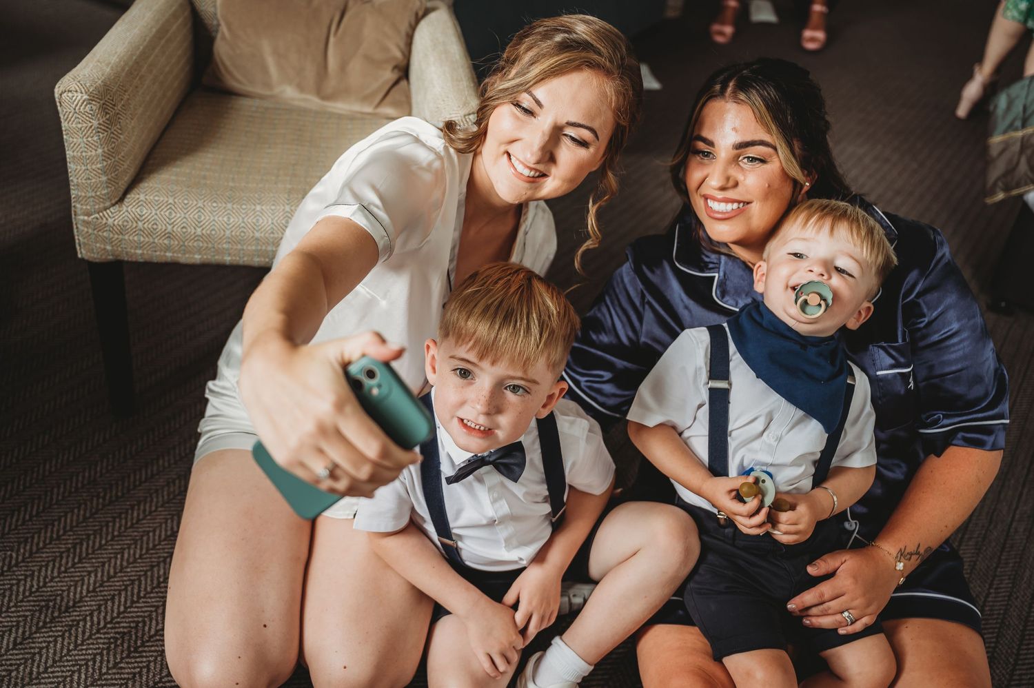 A happy family in matching formal attire sits together on the floor for a casual indoor photo.