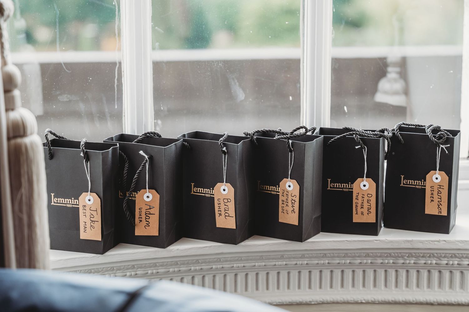 Row of black paper coffee bags with brown kraft tags lined up on window sill in natural light.