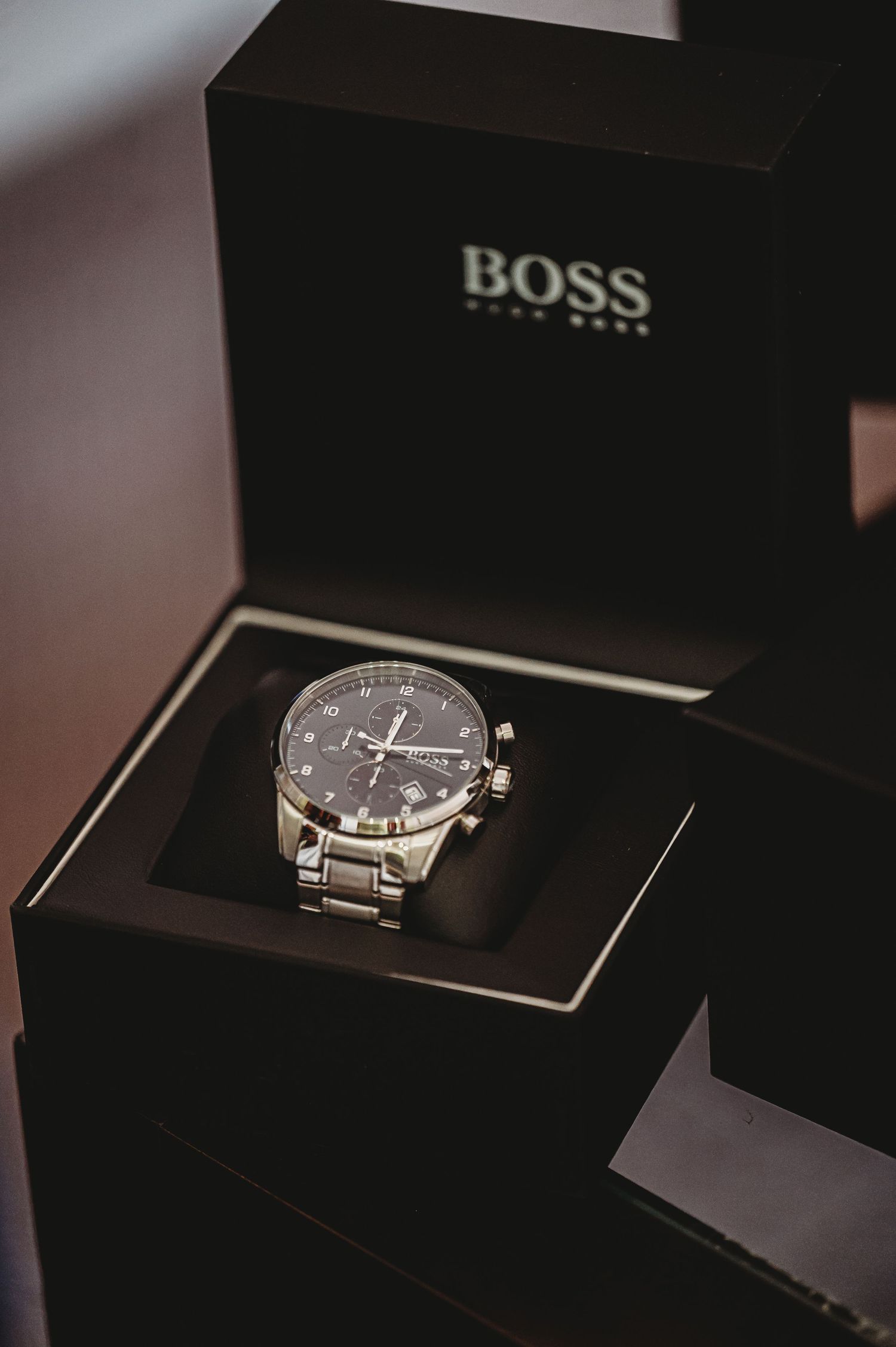 A luxurious Hugo Boss chronograph watch with silver bracelet sits in a black presentation box.