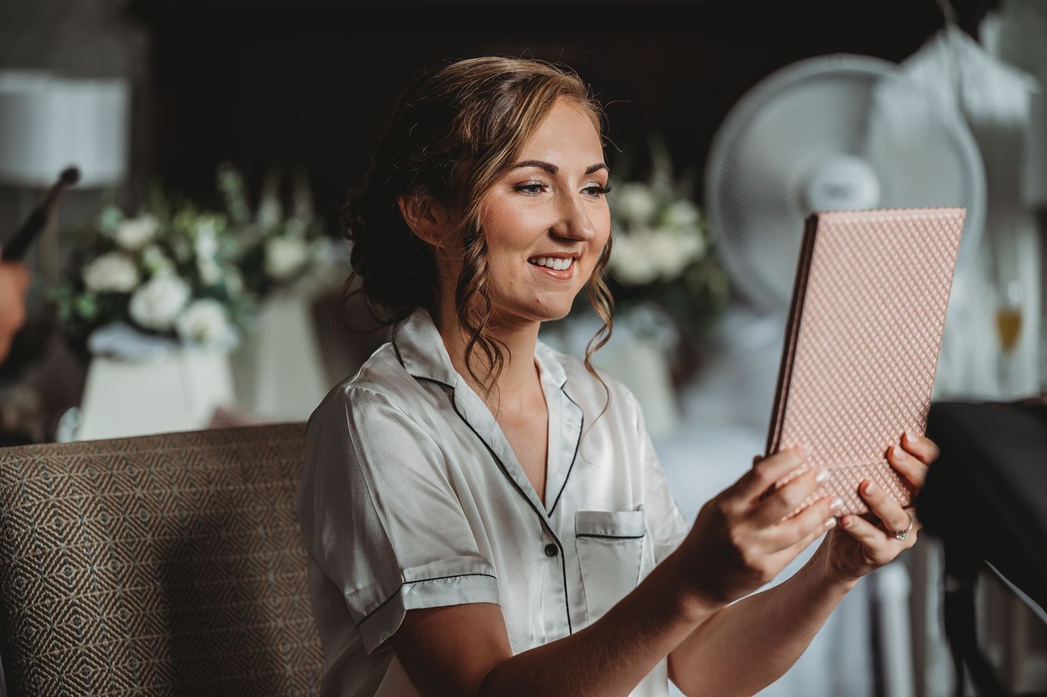 Woman in white shirt relaxing in wicker chair while reading on a digital tablet in cozy setting.