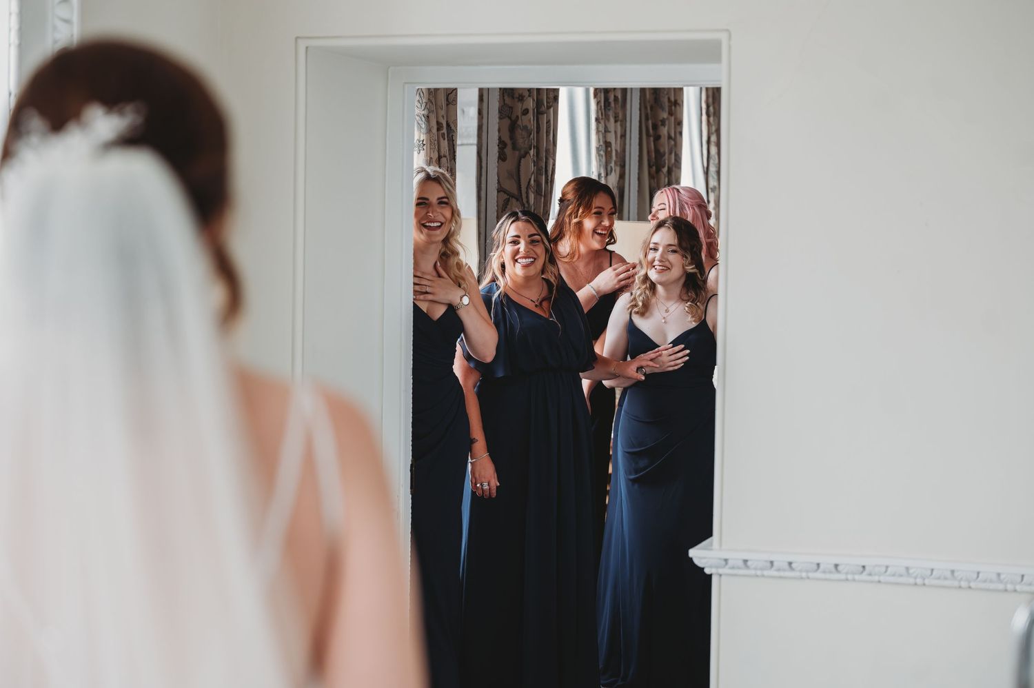 A group of people in navy dresses react emotionally while watching someone in a wedding veil.