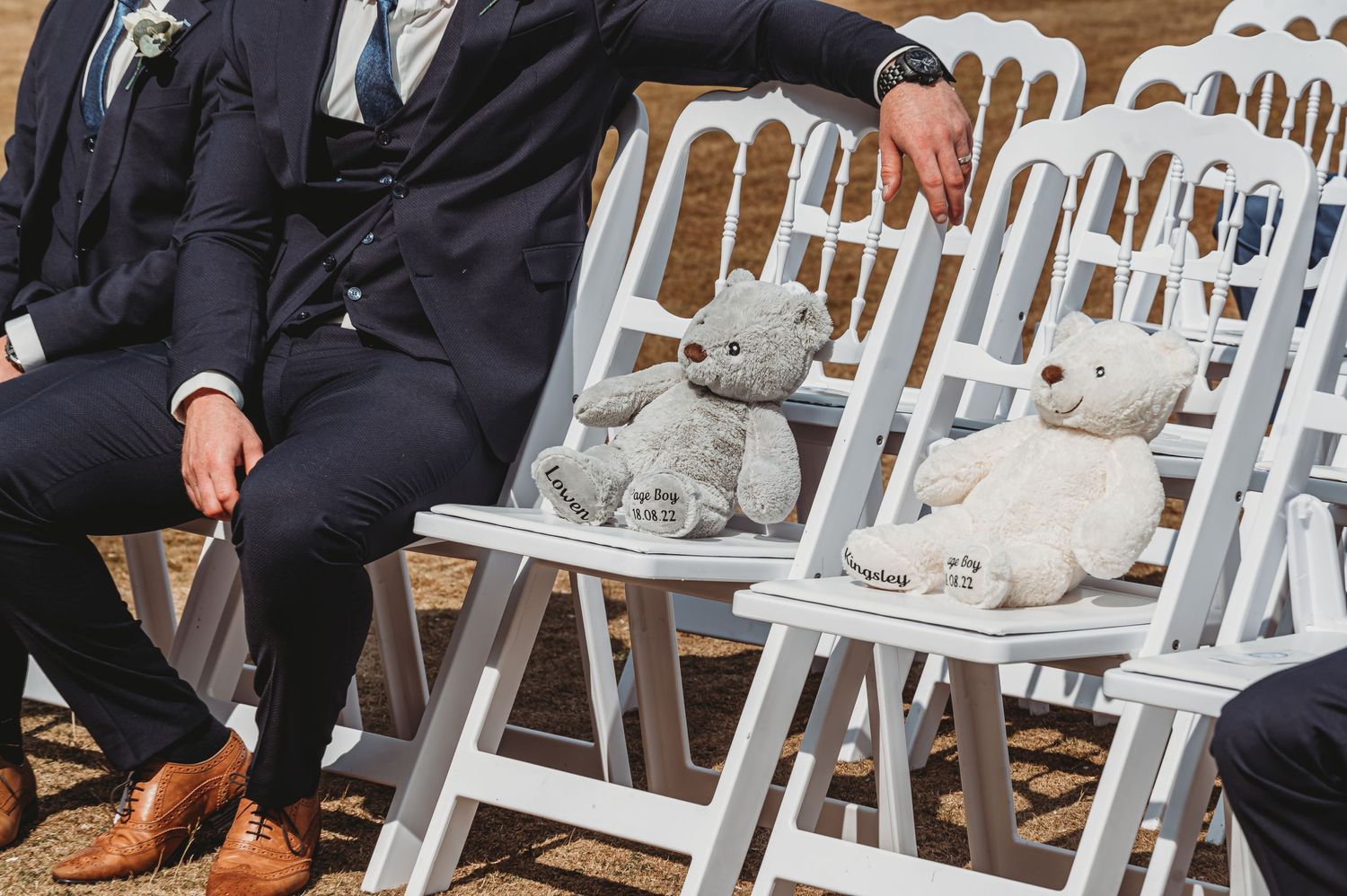 Decorative stuffed bunnies sit on white chairs at an outdoor ceremony while an attendee in a dark suit rests nearby.