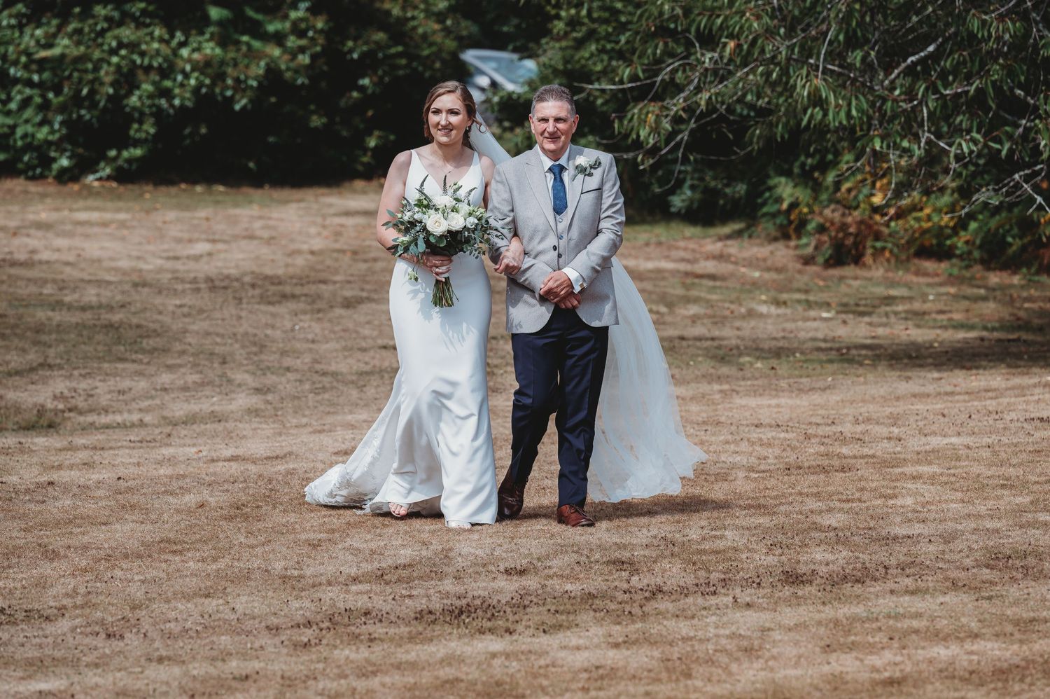 A happy couple walking together after their wedding ceremony, wearing a white lace gown and light grey suit.