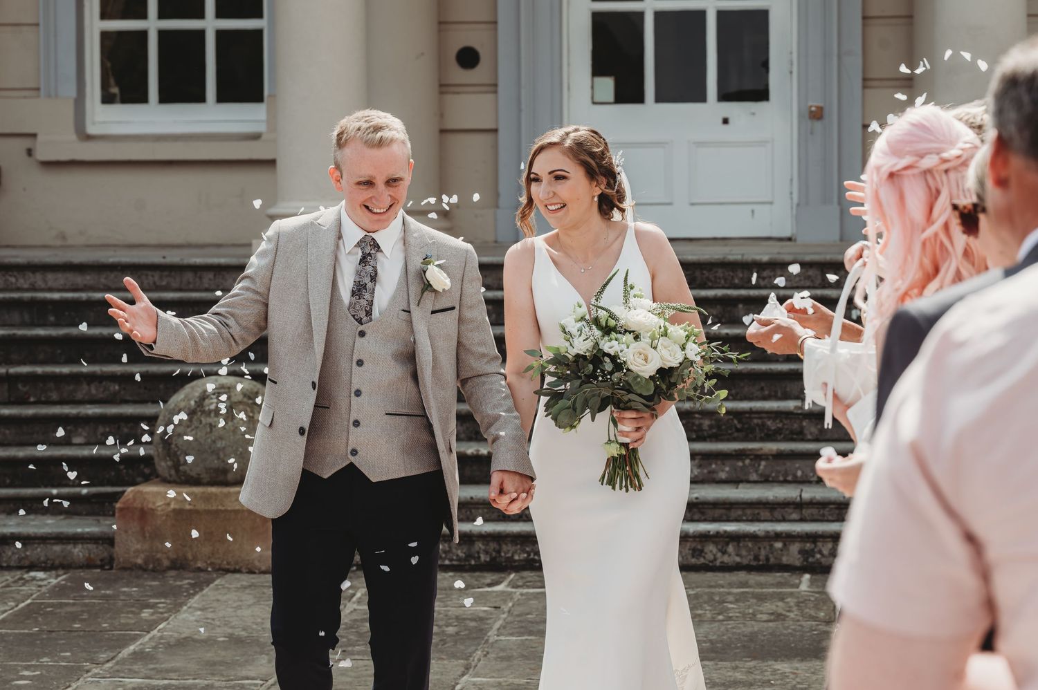 Wedding couple walking down stone steps while guests throw confetti on their happy celebration exit.