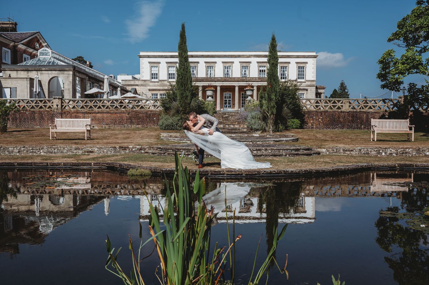 Elegant white mansion with cypress trees and reflection in still pond on wedding day at historic estate setting.