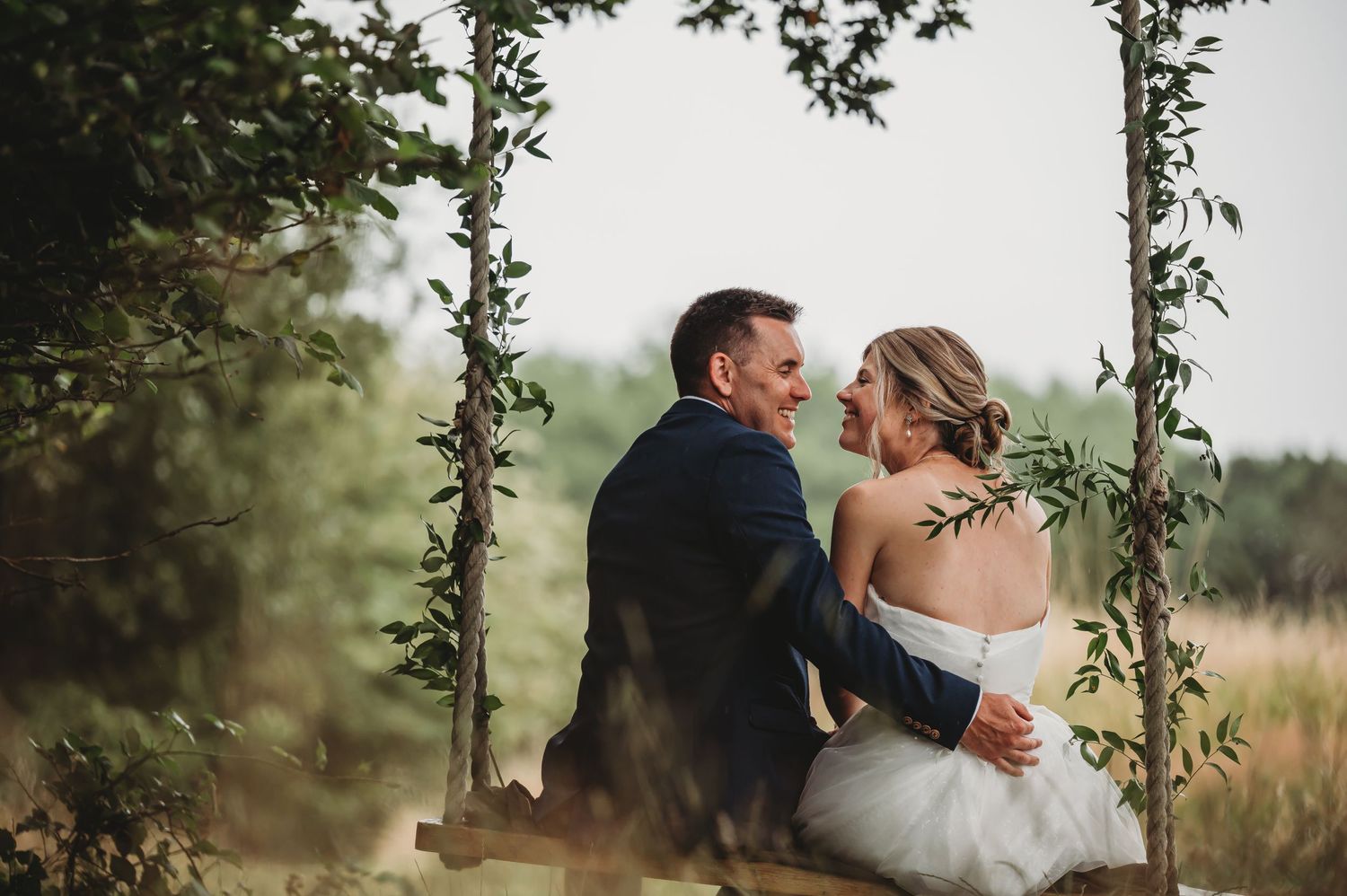 An intimate wedding portrait captured between vine-covered posts in a natural outdoor setting.