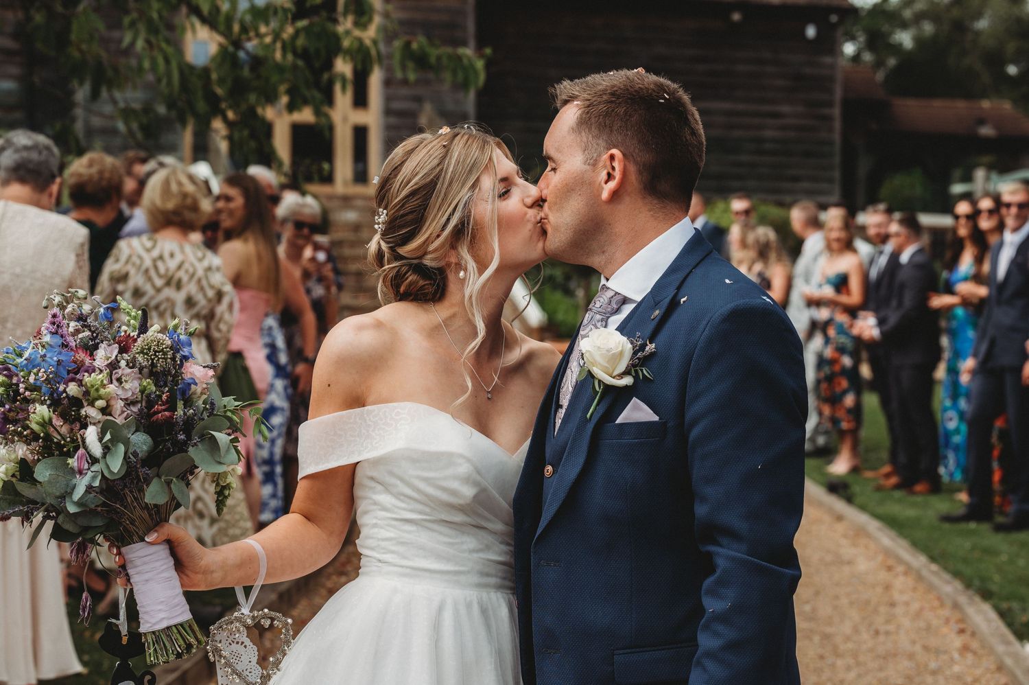 A romantic outdoor wedding moment with floral arrangements and guests in the background.