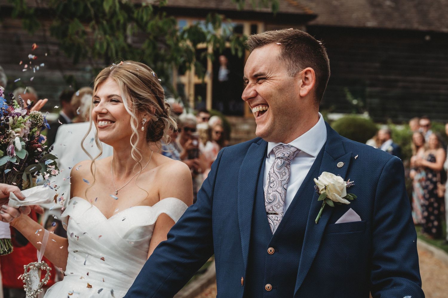 A joyful newlywed couple celebrates during their outdoor wedding ceremony as guests throw confetti behind them.