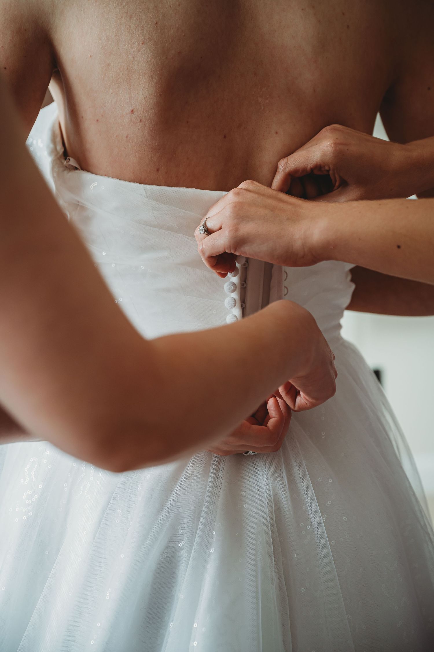 Close-up detail shot of hands fastening the back of a white wedding dress.