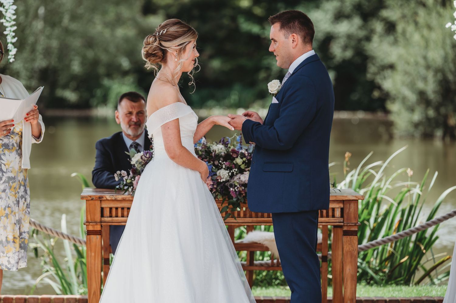 Bride and groom share a moment during their lakeside wedding ceremony with floral decorations.