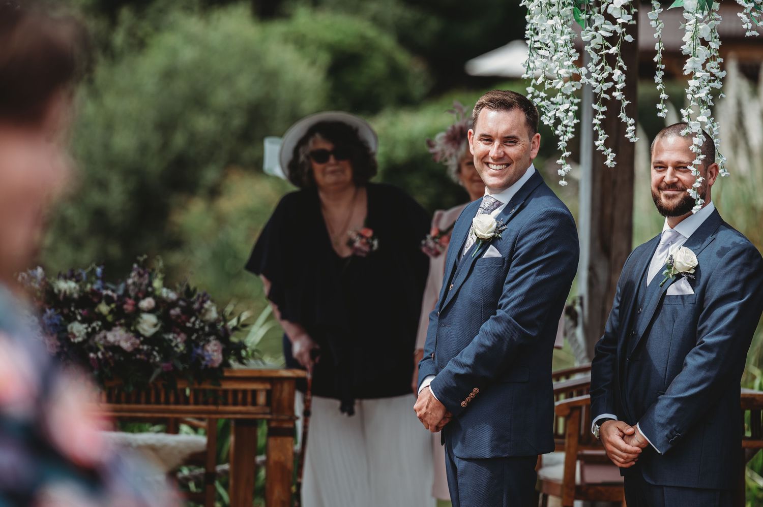 Wedding ceremony at an outdoor garden venue with floral arch decorations and guests standing at the altar.