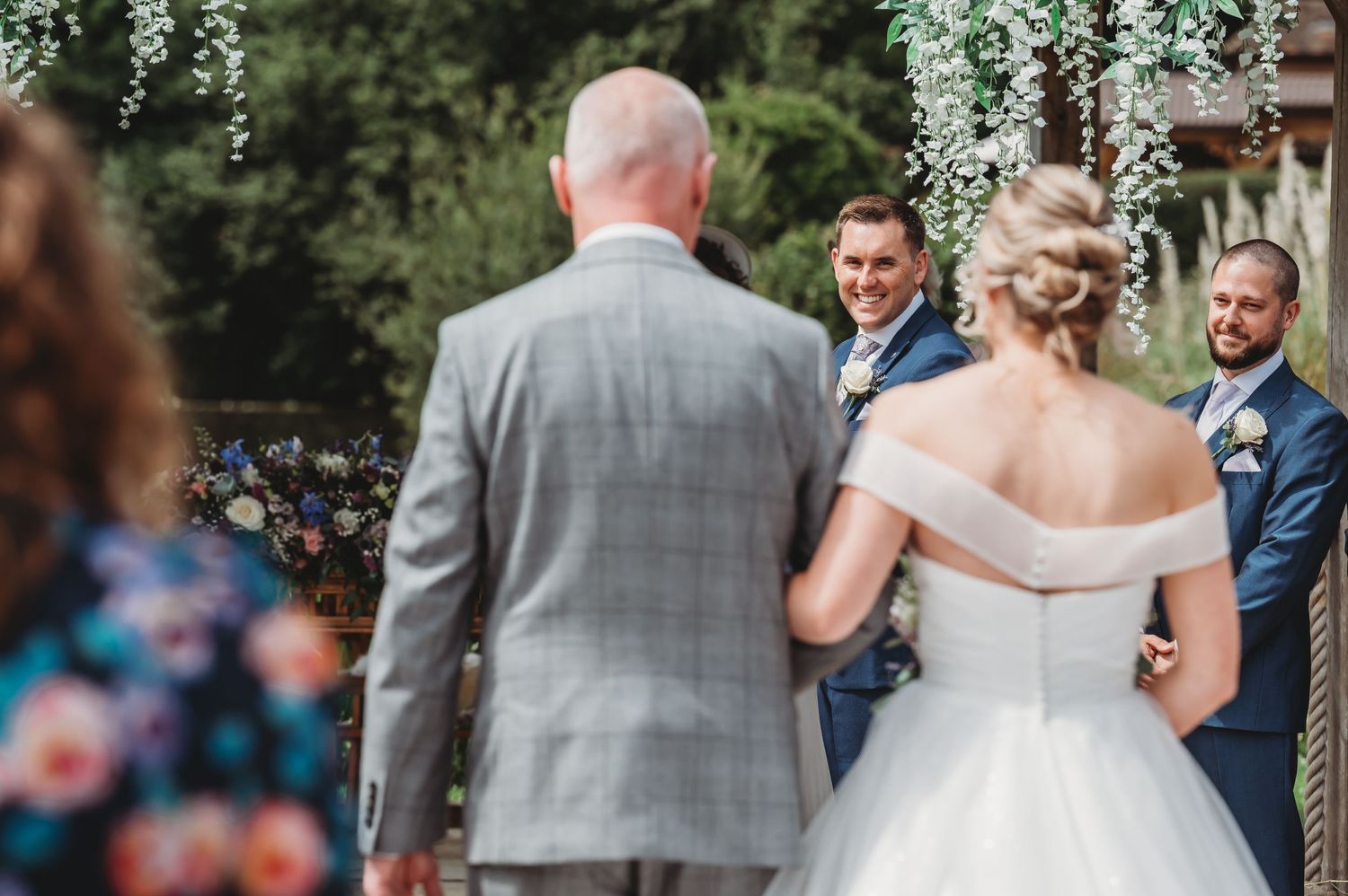 Wedding ceremony under hanging floral decorations with guests in attendance.