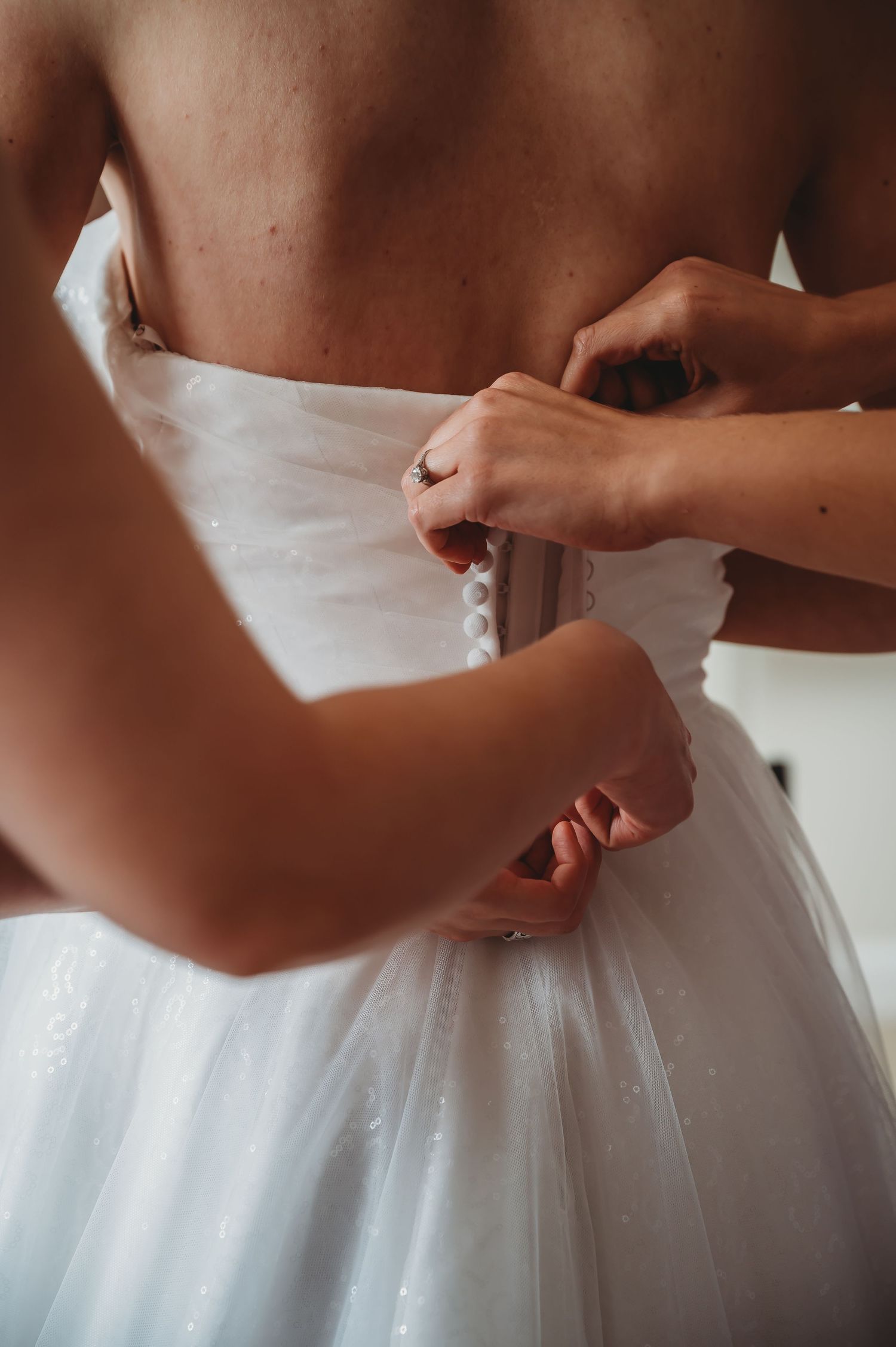 Hands lacing up a white wedding dress corset back against soft natural lighting.