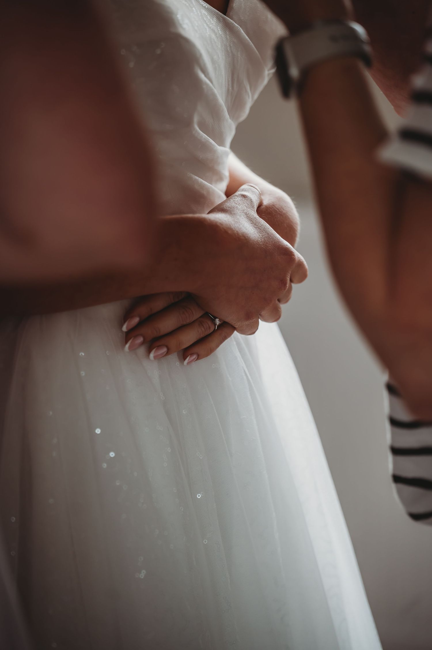 Close-up detail of hands and white wedding dress fabric with sparkly details.