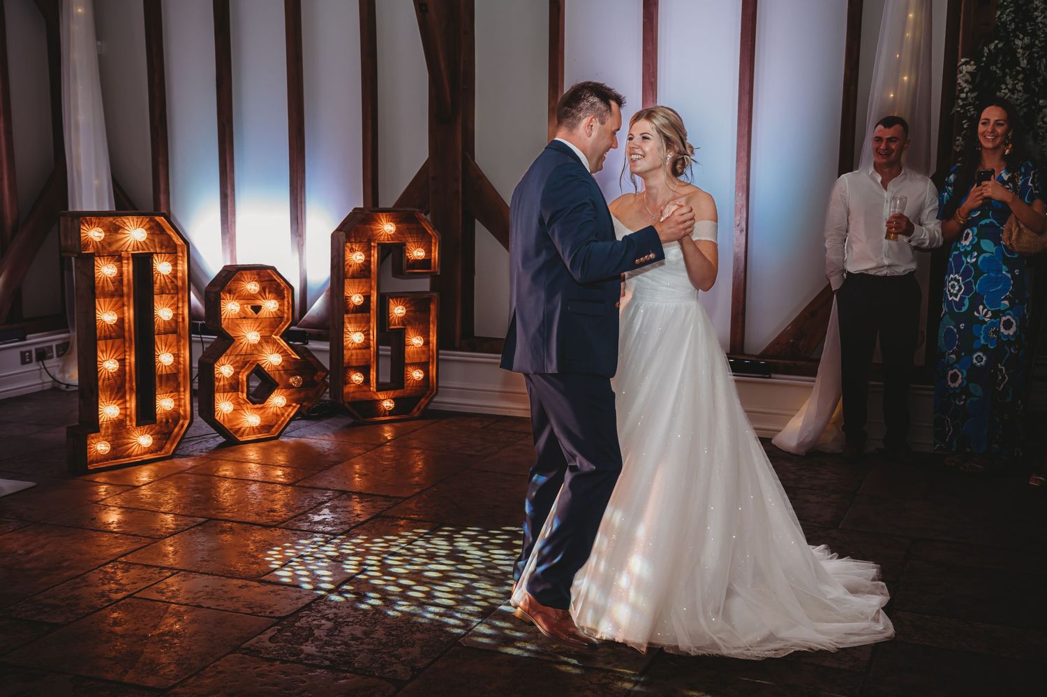Couple shares their first dance under illuminated marquee letters in a rustic venue.