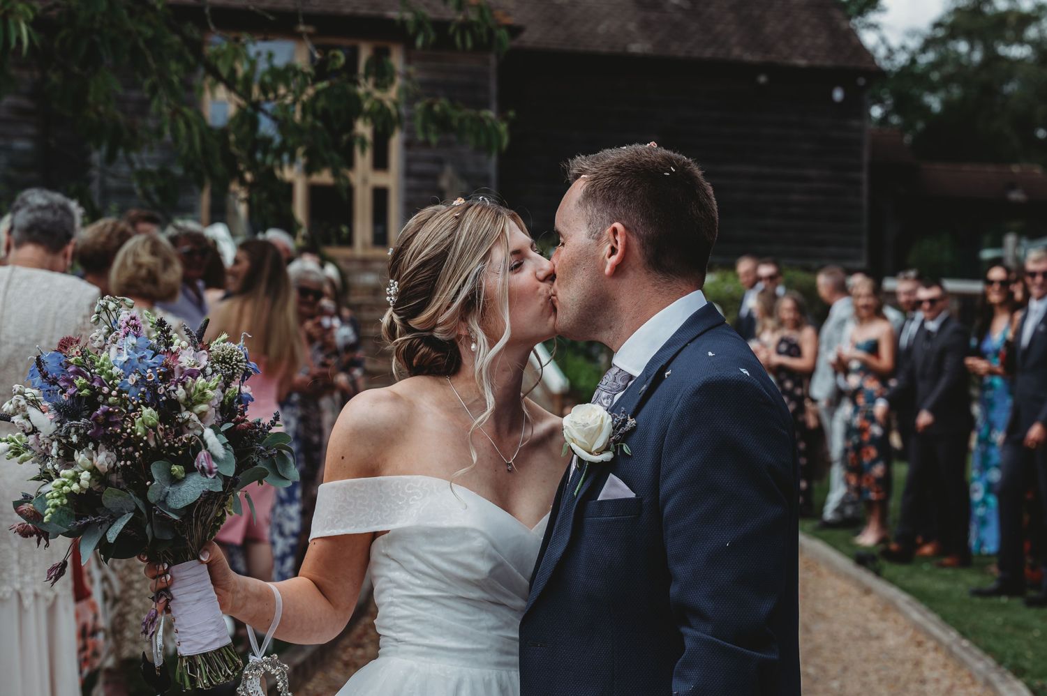 A newlywed couple shares an intimate moment during their outdoor garden ceremony while holding a wildflower bouquet.
