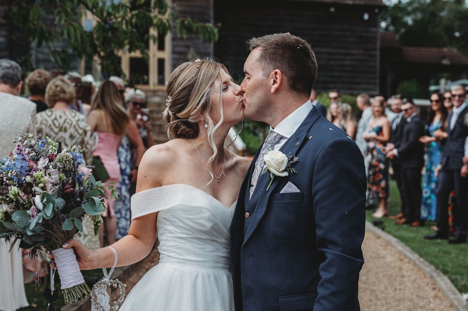 A romantic outdoor wedding moment as the couple shares a kiss while holding a beautiful floral bouquet.