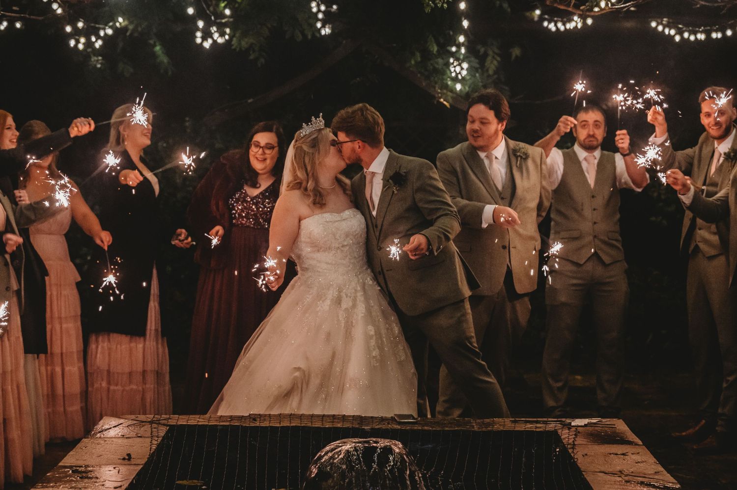Wedding party celebrates with sparklers during nighttime reception festivities.