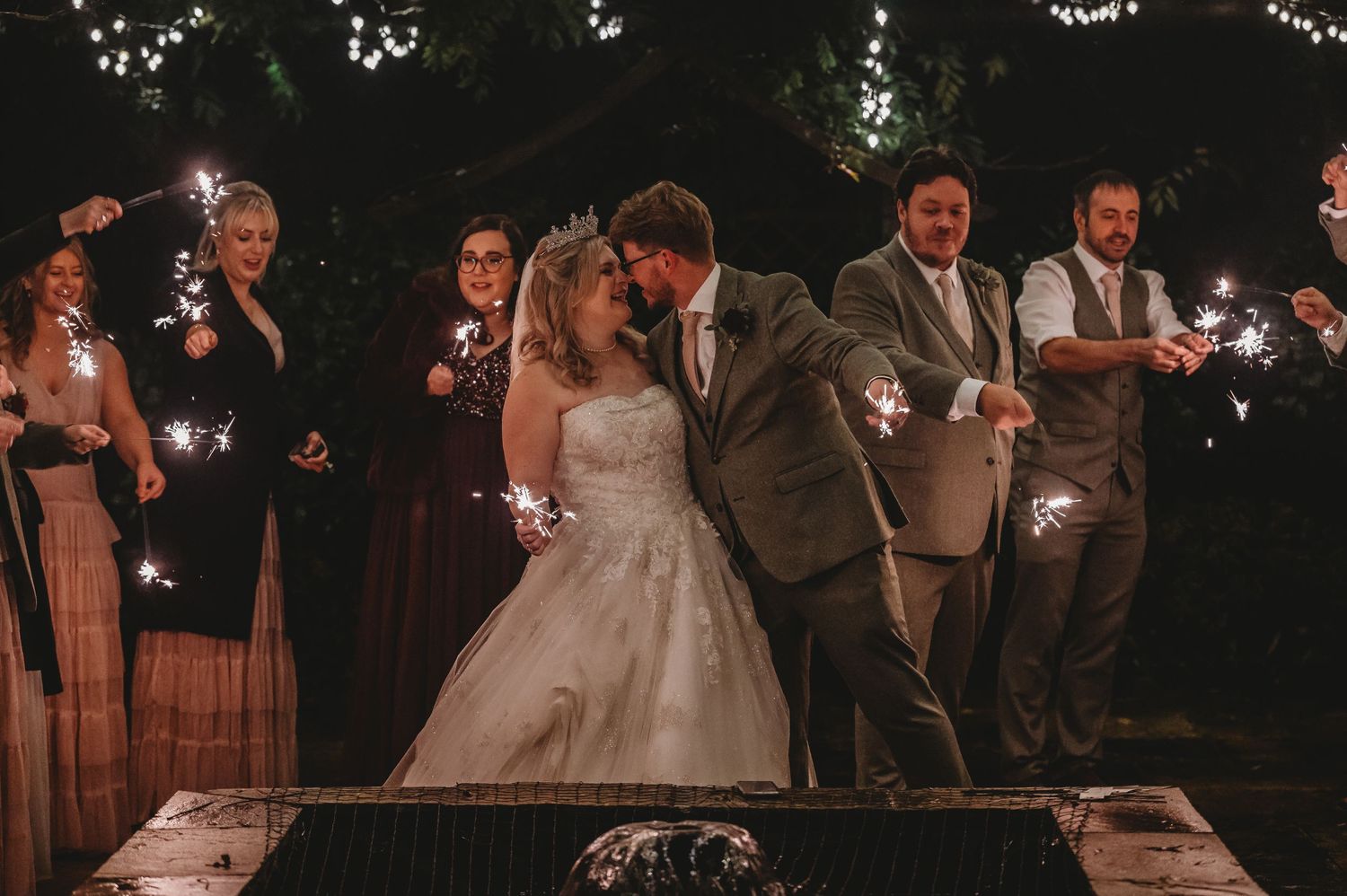 Newlyweds dance together surrounded by sparklers and guests during evening wedding celebration.