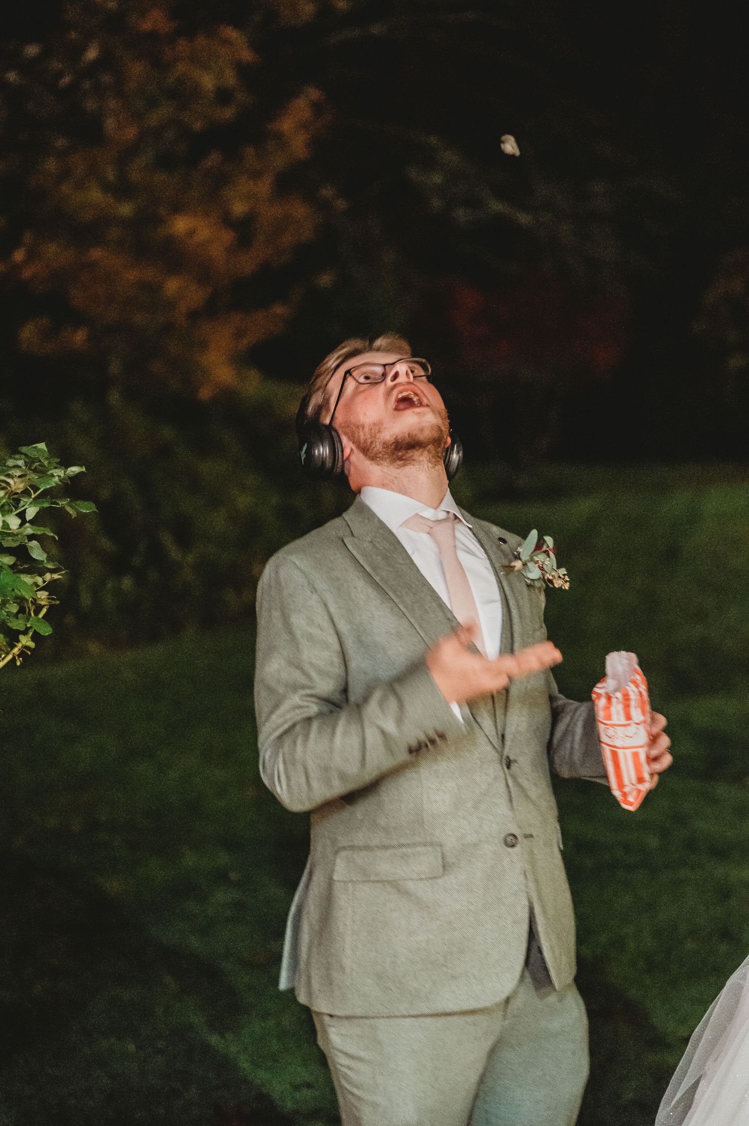 Wedding guest in gray suit dancing outdoors at night while holding a drink.