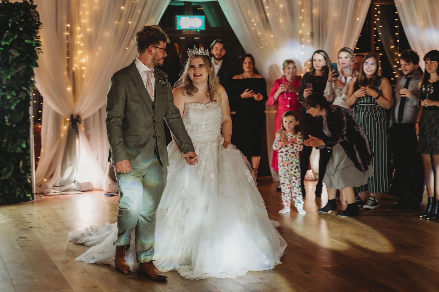 A couple shares their first dance at a wedding reception surrounded by twinkling lights and white drapery.