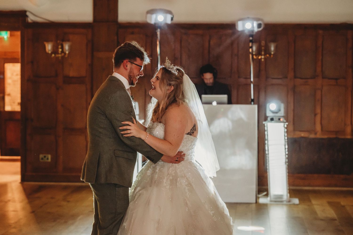 Couple sharing an intimate moment during their first dance in a wood-paneled reception hall.