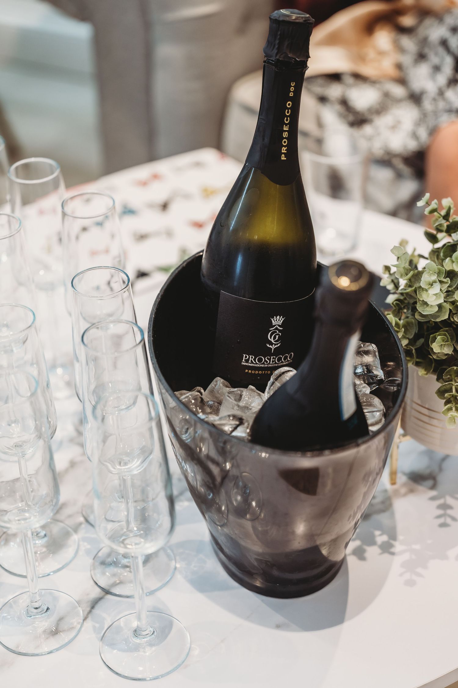 Wine bottles chilling in an ice bucket with empty champagne flutes on a white tablecloth.