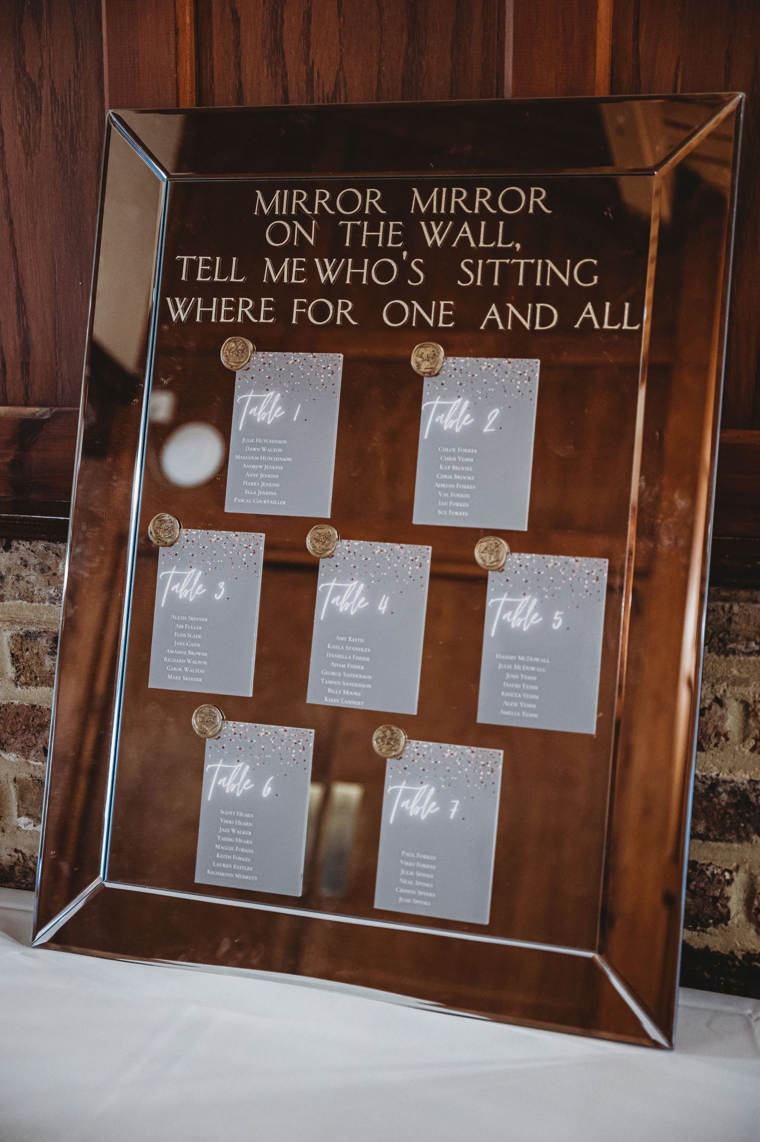 Mirror-framed seating chart display with 'Mirror Mirror on the Wall' theme for wedding table assignments.