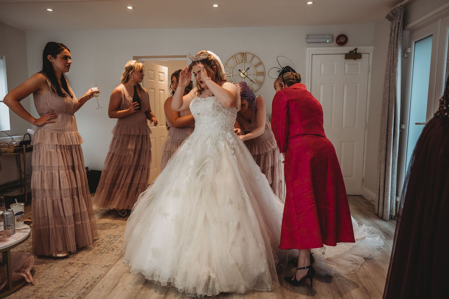 Wedding preparation scene showing bride in white gown surrounded by attendants in mauve dresses.