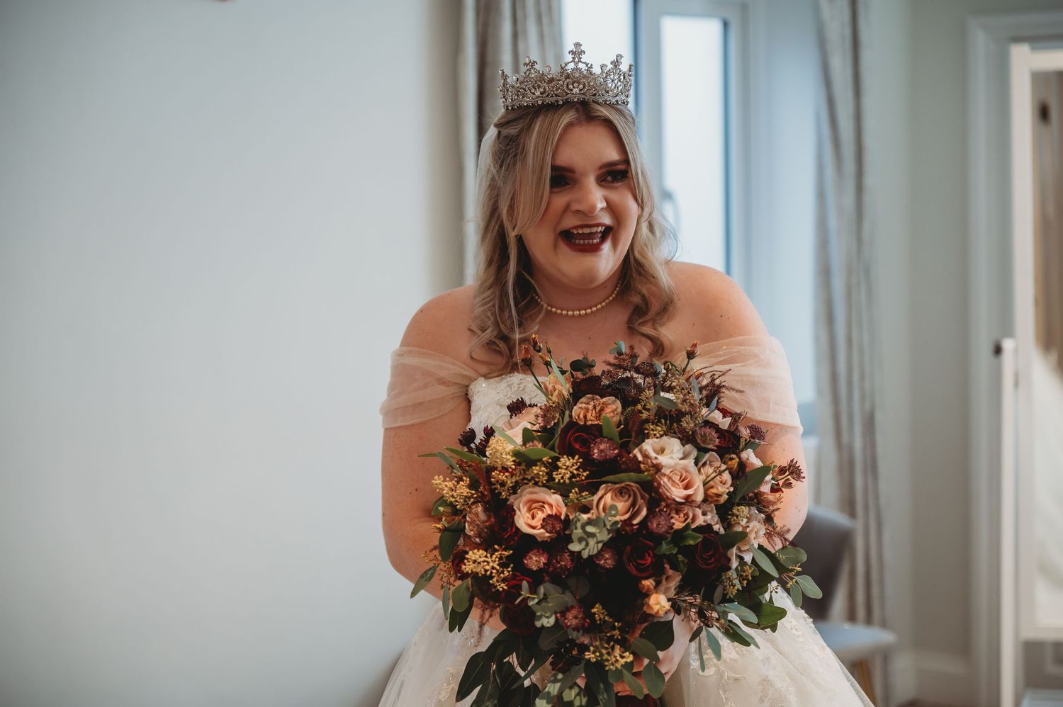 Bride in white gown holds stunning autumn-toned bouquet in elegant indoor setting.