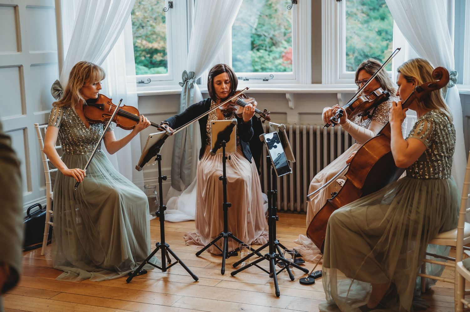 String quartet of musicians in matching sage dresses performs at an elegant venue.