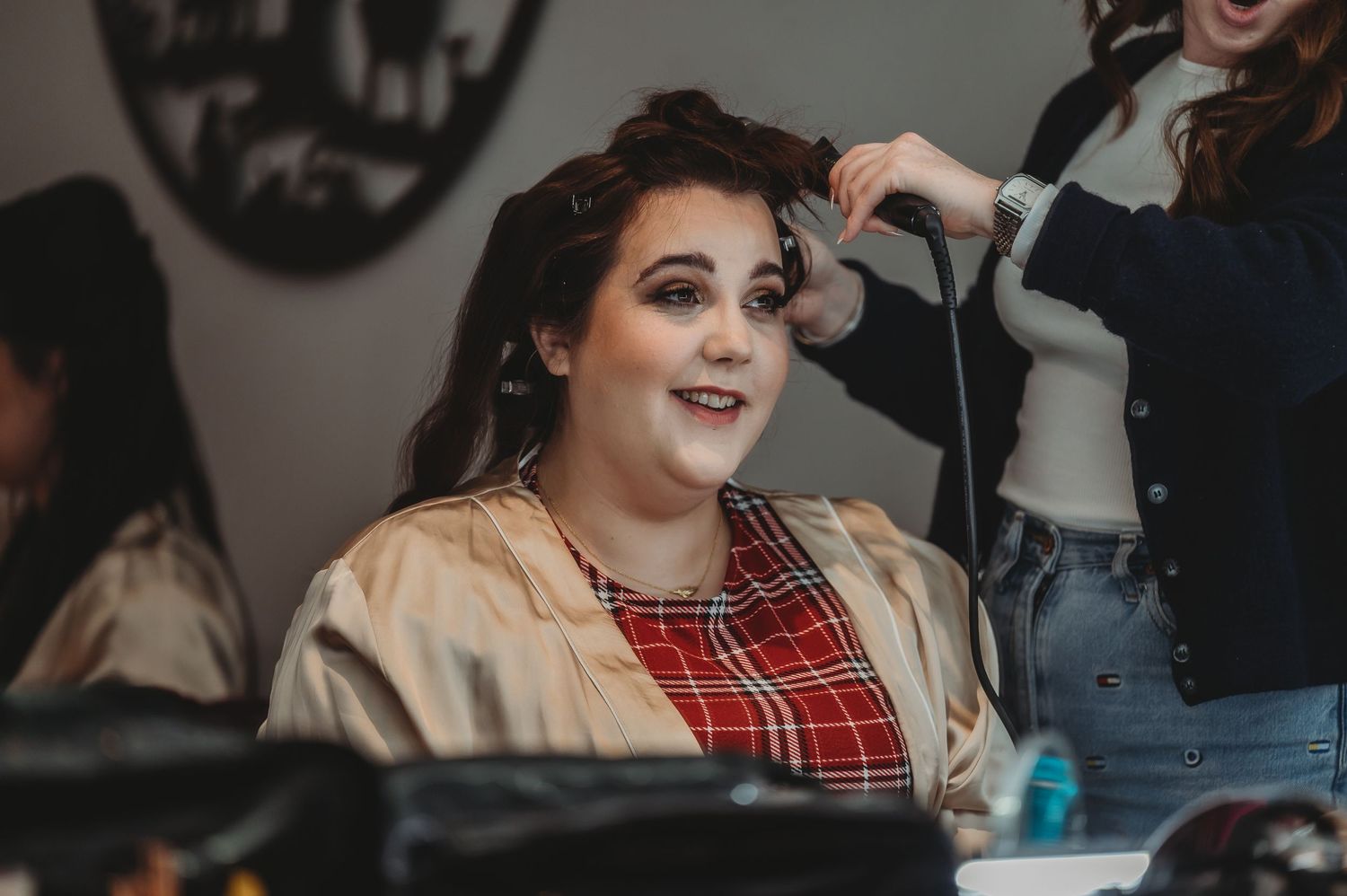 Someone getting their hair styled while wearing a plaid top and beige jacket.