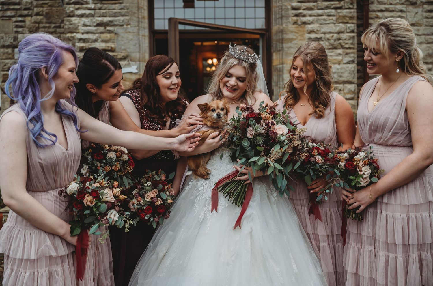 Wedding party in pastel dresses admiring small pet during photo session.