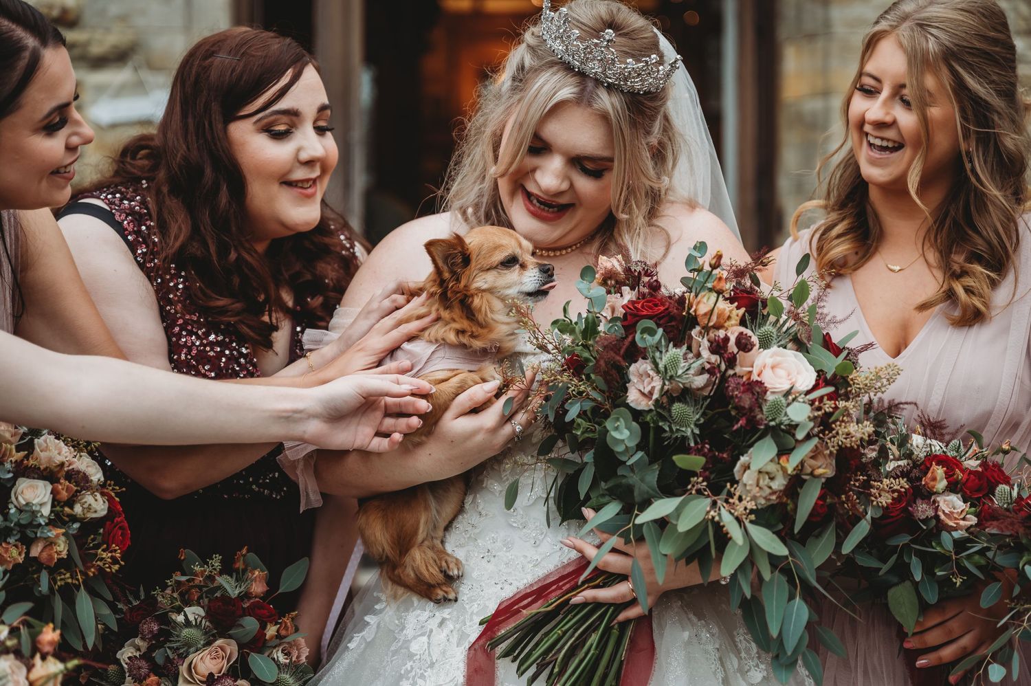 Bridesmaids in pink dresses gather around small dog and bouquets.