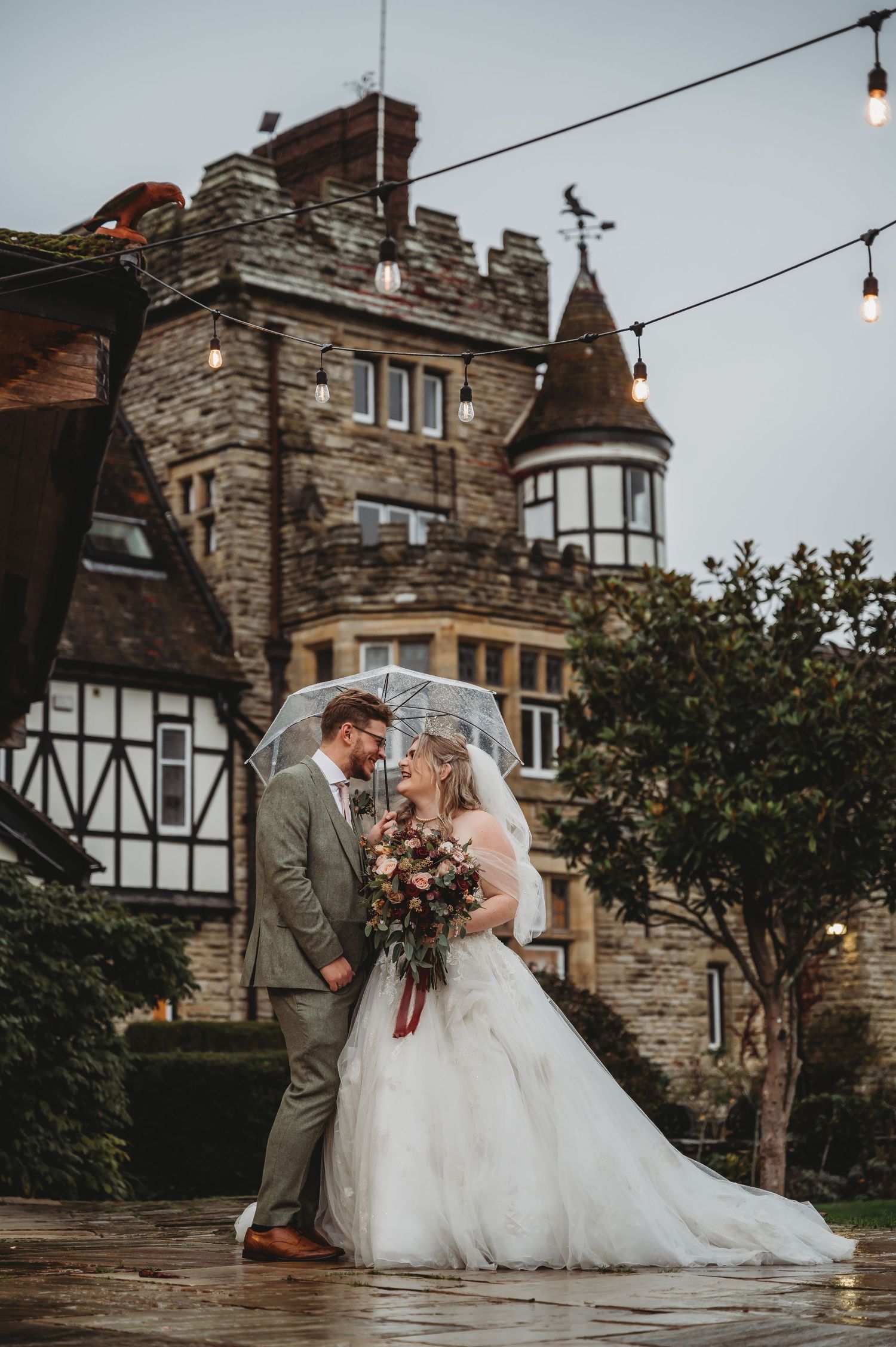 Elegant wedding portrait against backdrop of stone castle on rainy afternoon.