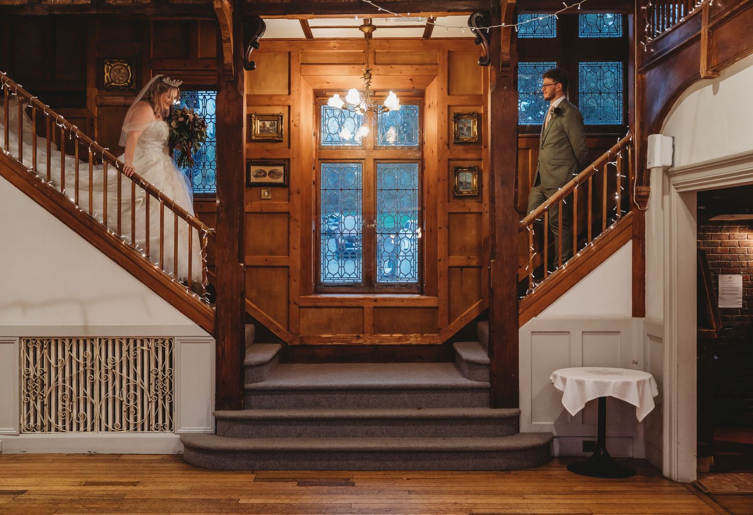 Interior wooden staircase with stained glass windows in rustic venue illuminated by natural light.