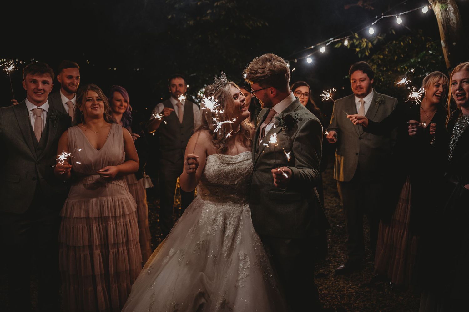 Wedding party gathers under string lights for evening celebration.