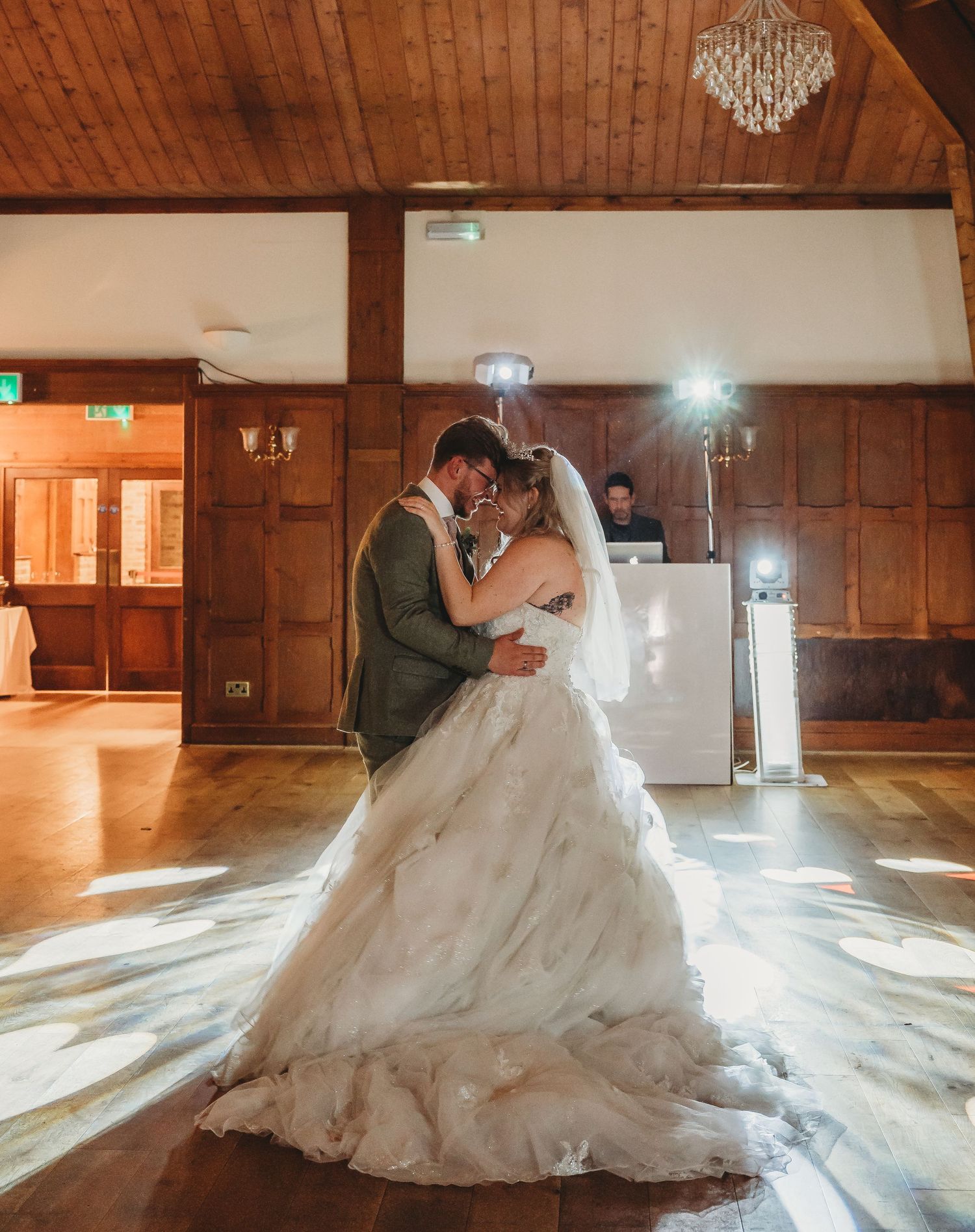 A couple shares an intimate moment during their first dance in a wooden-beamed reception hall.