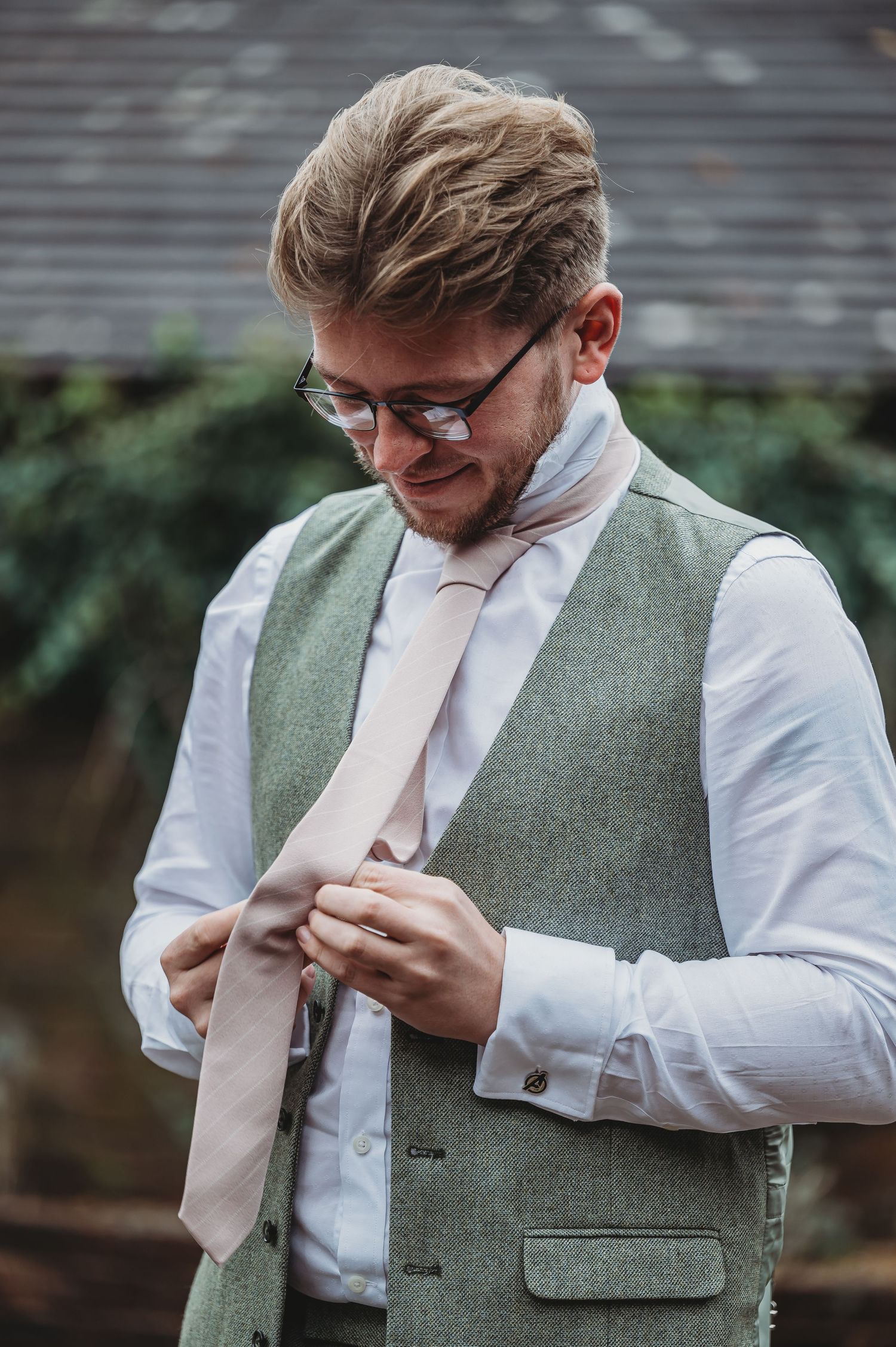 Someone adjusts their pink tie while wearing a sage green vest and white dress shirt.